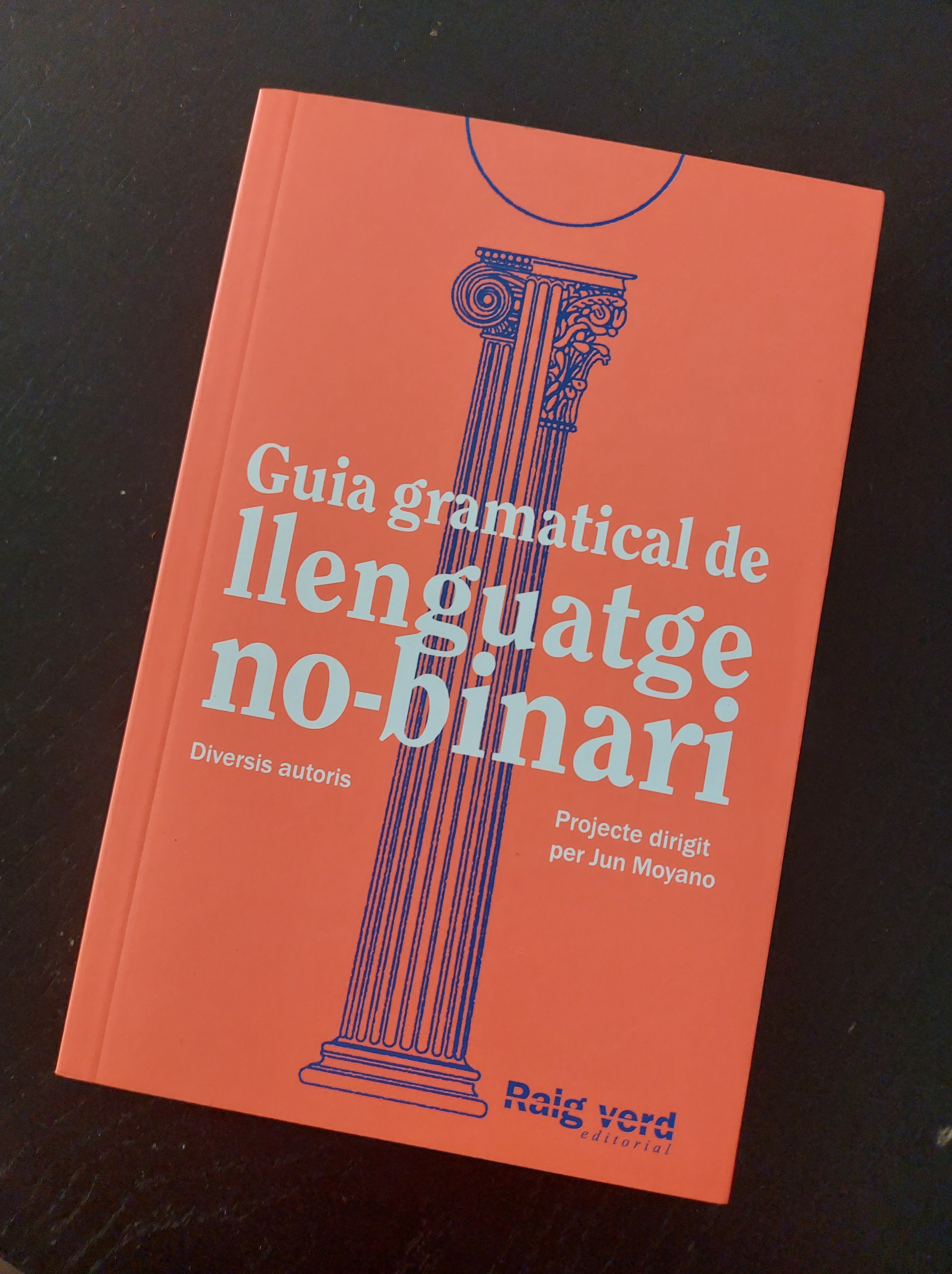 Llibre "guia gramatical de llenguatge no-binari". Te la coberta taronja fluorescent amb una columna que mescla els 3 estils grecs en blau mari i el títol en lletres blanques.